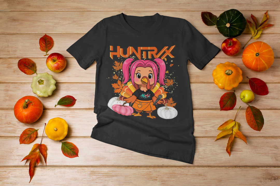 Black t-shirt with a cartoon character and 'HUNTRX' text on a wooden surface with autumn decorations.