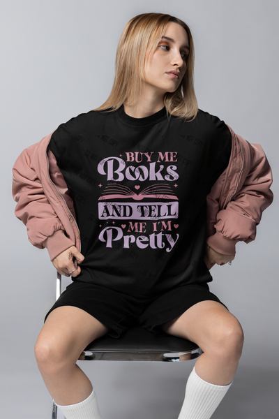 A person wearing a black T-shirt with the text 'Buy Me Books and Tell Me I'm Pretty' in pink and purple colors.